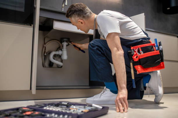 istockphoto-1360492244-612×612 Eliminating problem. Middle aged man in t-shirt and overalls kneeling with wrench touching pipe under sink in lighted kitchen